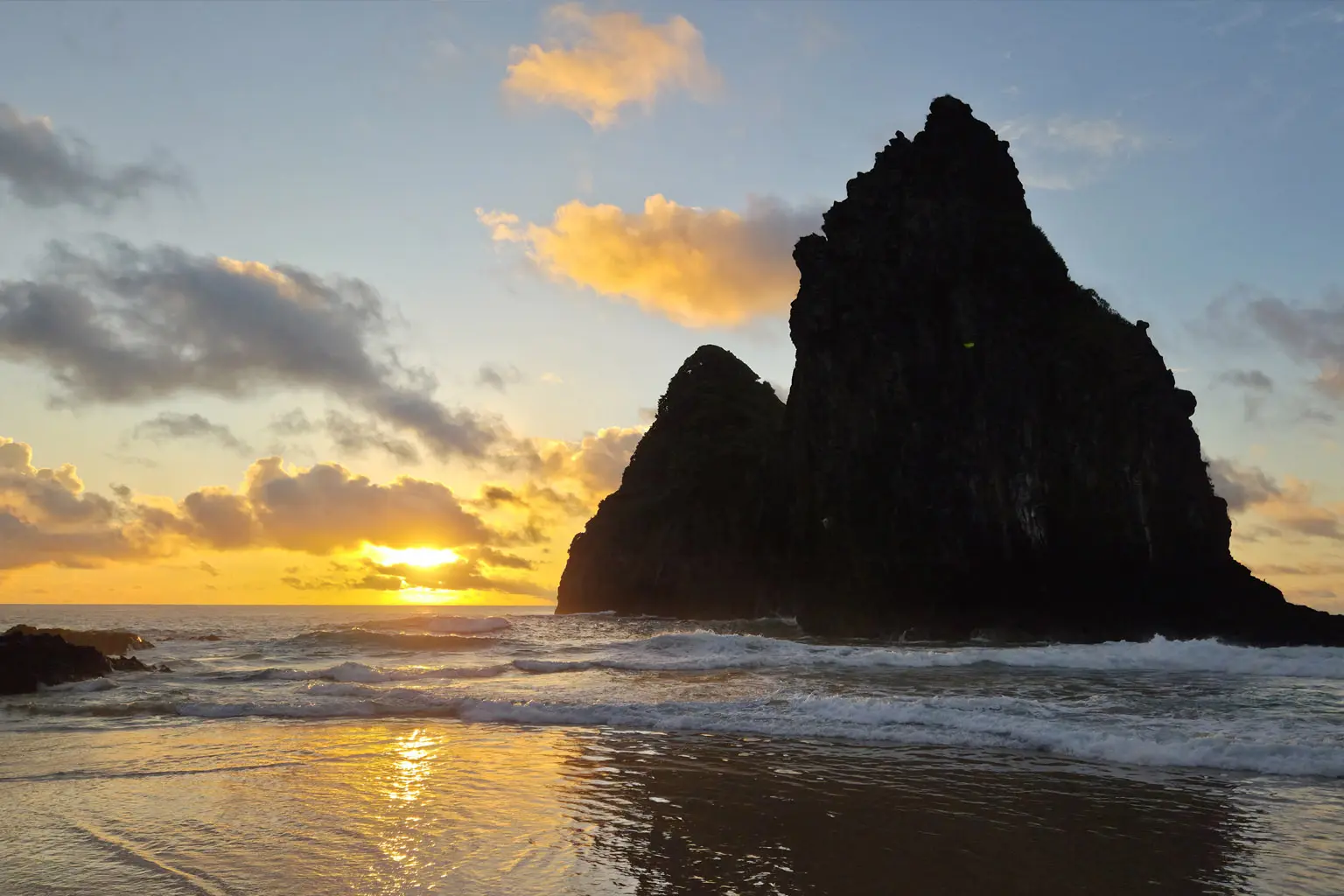 Pôr do sol dourado atrás de formação rochosa em Fernando de Noronha